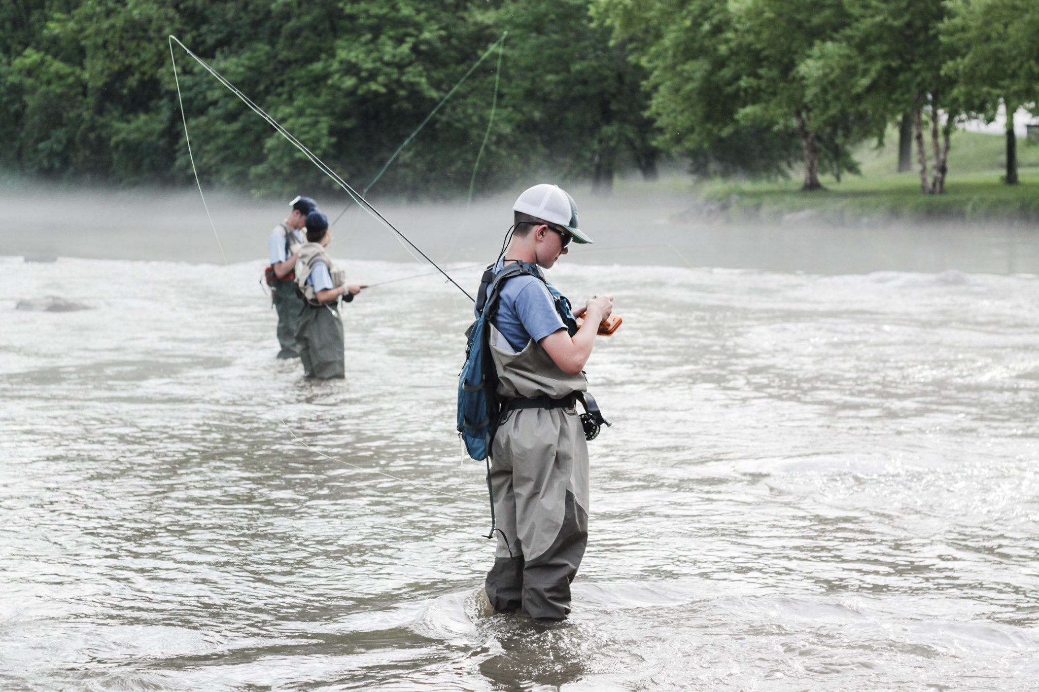 Three young anglers standing in a stream fly fishing.