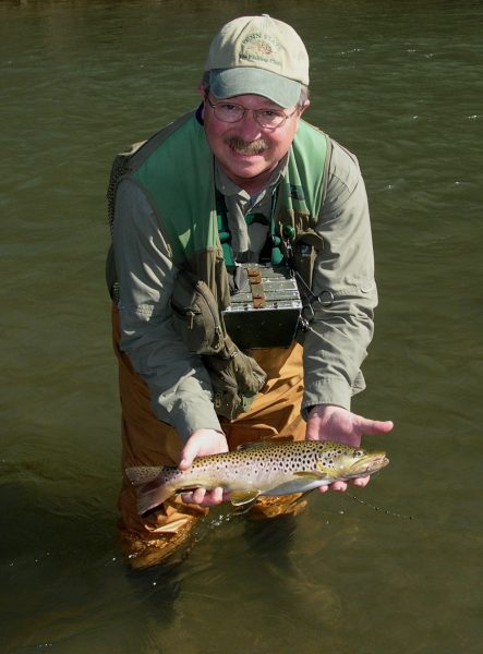 Greg Hoover standing in a stream holding a brown trout.